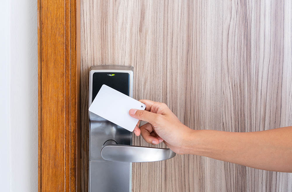 Closeup hand of young Asian woman using a keycard to unlock electronic sensor of hotel door. Security concept.